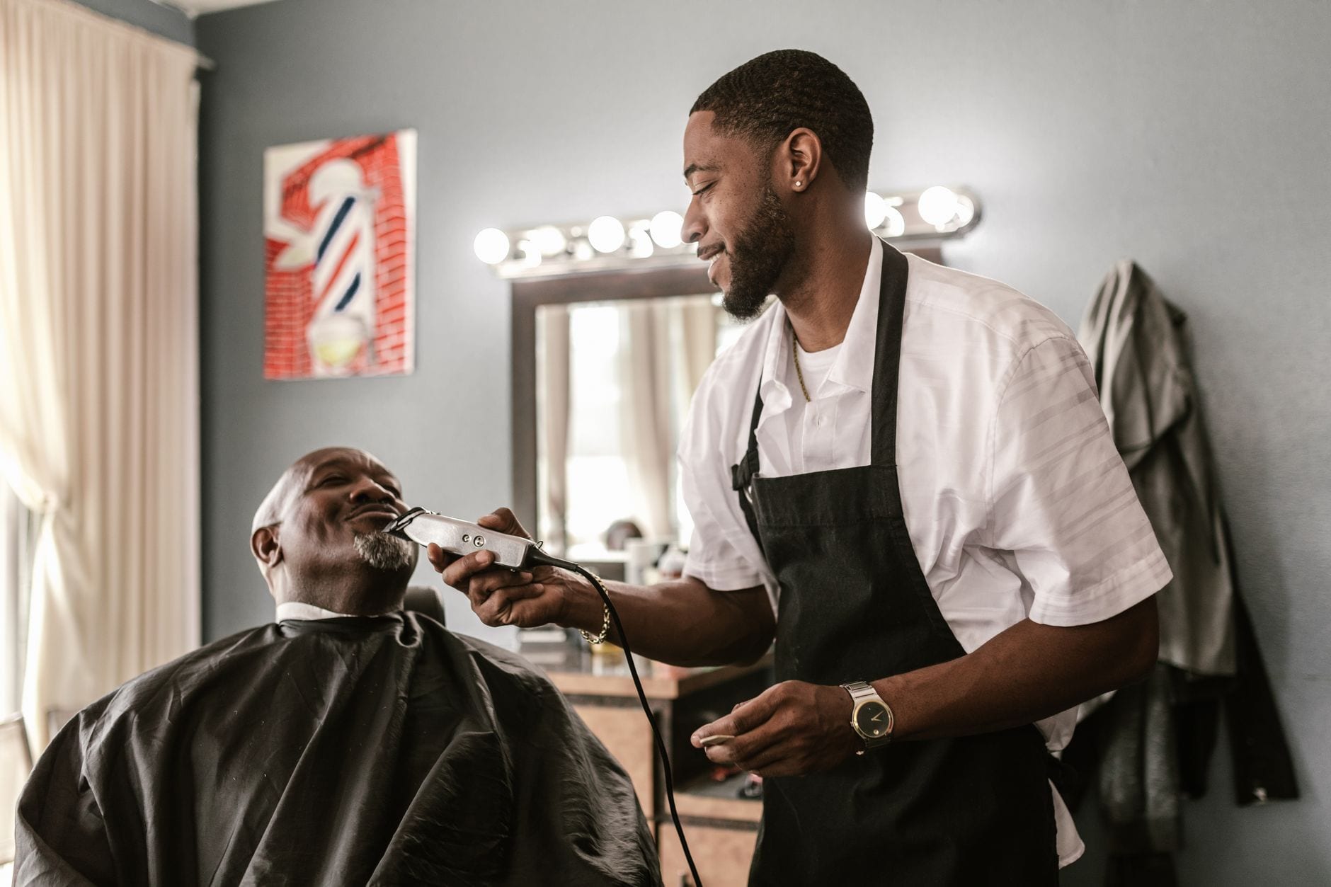 A barber trimming a client's beard with clippers in a barbershop